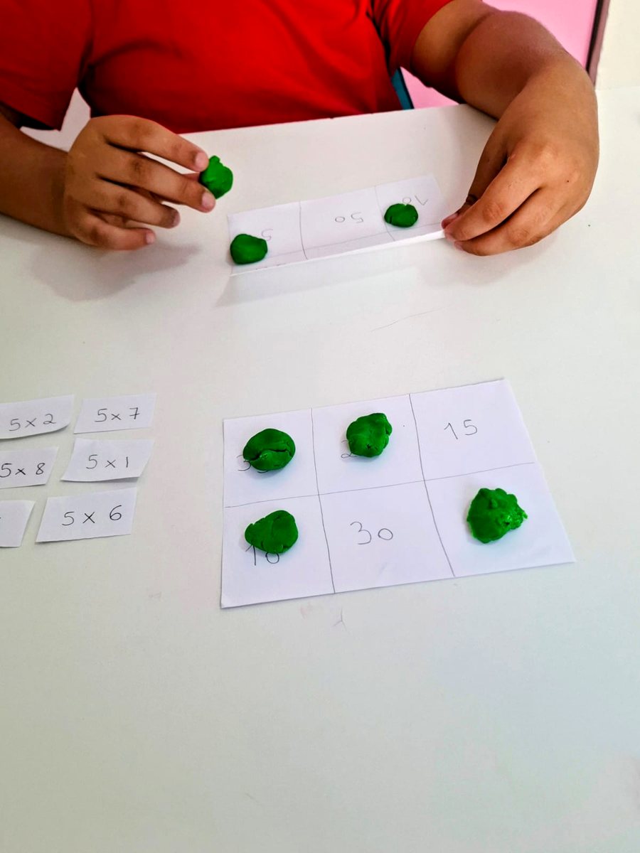 Atividade de multiplicação com cartelas e massinha verde sobre a mesa da clínica