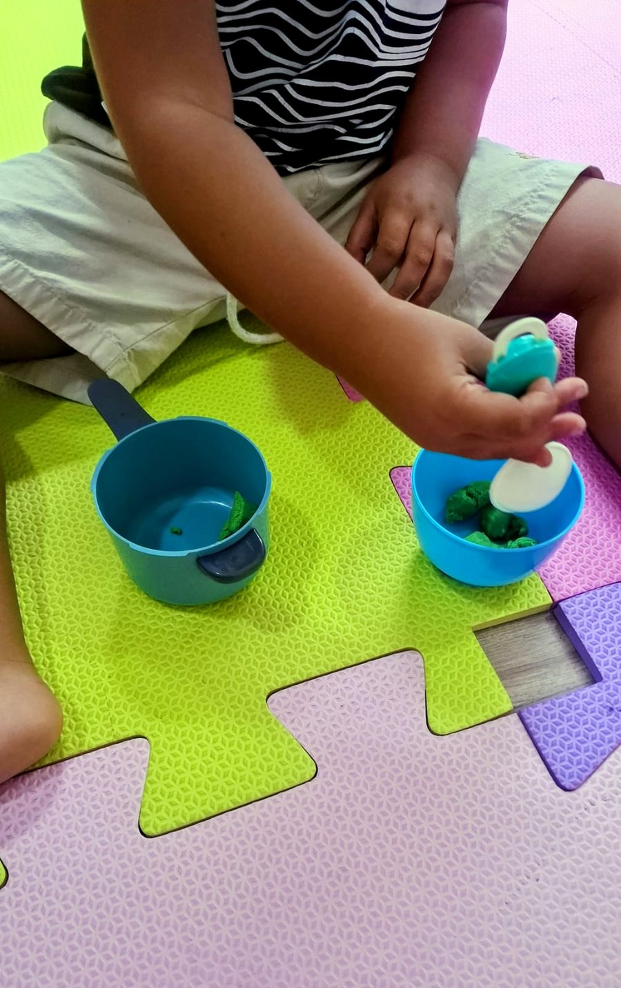 Criança pequena brincando com copos coloridos no tatame da clínica
