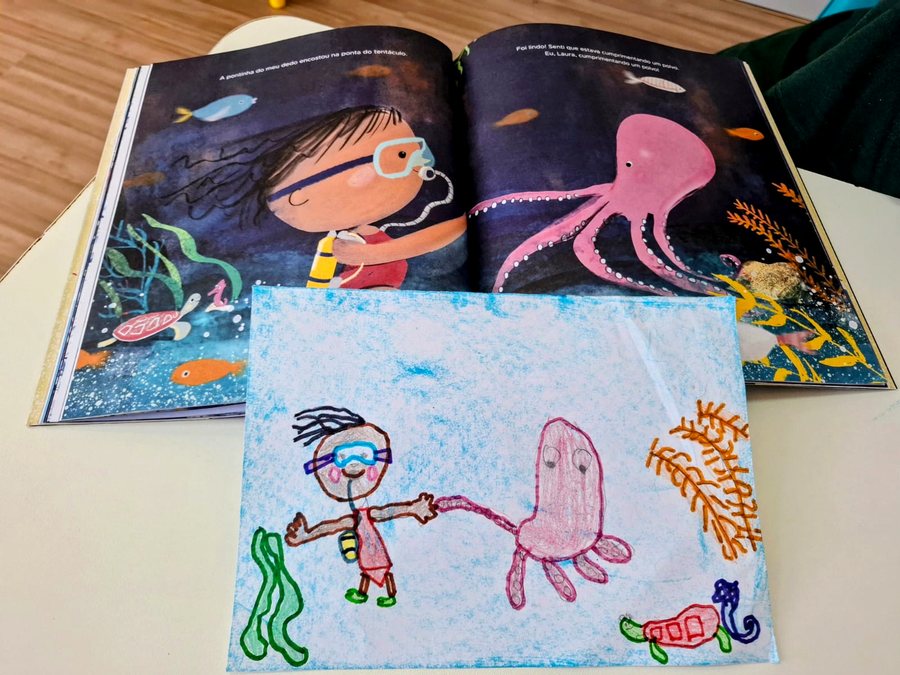 Livro ilustrado ao lado do desenho feito pela criança em uma atividade da clínica
