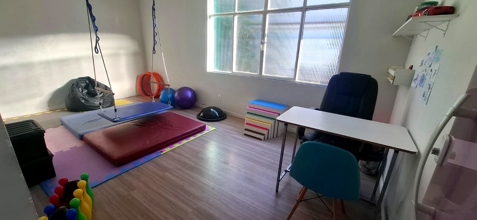 Sala de integração sensorial da clínica com balanço terapêutico, colchões e bolas